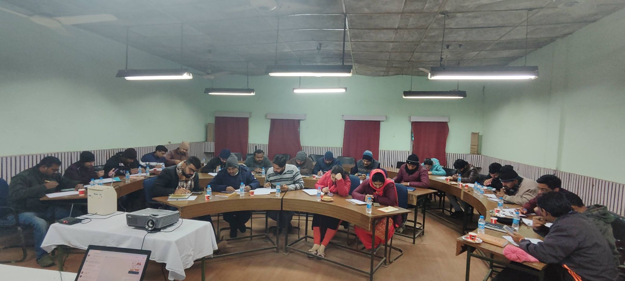 Participants seated in a U-shape arrangement during a QualityNexus training session, with projector and presentation laptop in the foreground